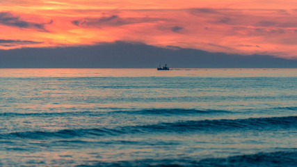 Fototapeta premium Sunset sky over the sea with a ship in distance.