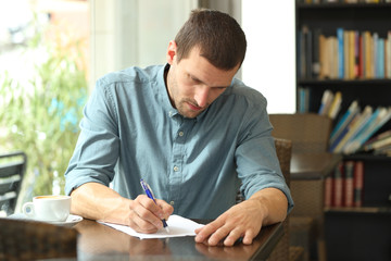 Concentrated man writing notes in a paper in a coffee shop