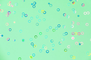 Colorful holographic foil confetti background. Pastel colored pink, blue and yellow circles sparse on trendy neo mint green colored paper. Simple holiday concept. Top view, flat lay