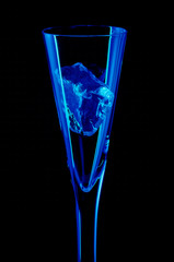 A fluted glass with a single ice cube in it and light with blue strip lights on a black background