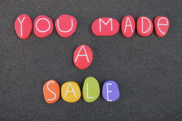 You made a sale, commercial phrase composed with multicolored stones over black sand