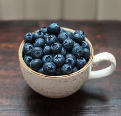 Fresh blueberries in a cup on a dark background. Side view, macro. Blue ripe berries closeup on a brown wooden background.