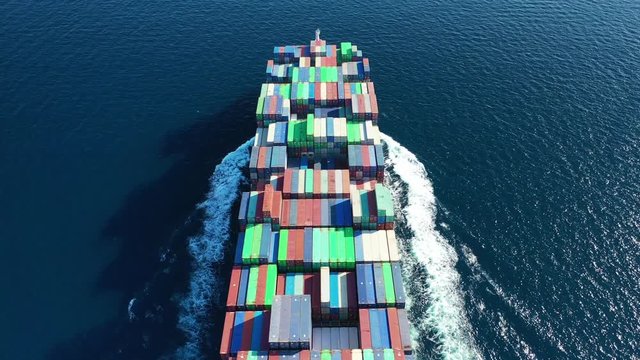 Aerial drone tracking video of Container cargo Ship carrying load in truck-size colourful containers cruising the deep blue Pacific ocean