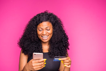 a beautiful young african nigerian lady feels happy what she is doing with her smart phone and credit card