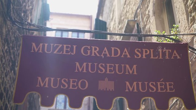 Walking under the name board of split city museum on Papaliceva Ulica, next to the Split City Museum.
