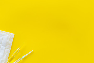 Influenza preventive tools. Medical face mask and vaccine on yellow background top view space for...