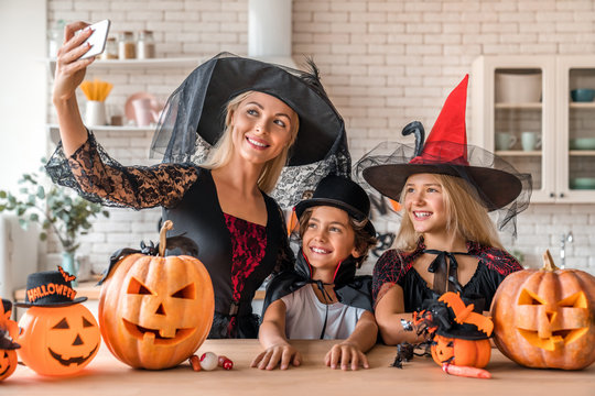 Smiling young woman taking selfie with her kids in Halloween decorated kitchen