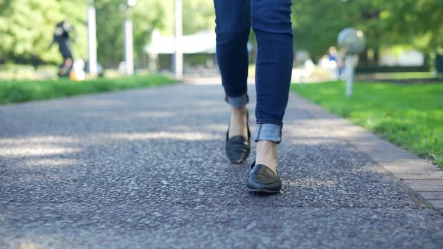 Low angle shot of Young woman walking outside in city park during the day. Focused only on the feet and shoes with shallow depth of field 