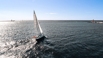 Aerial photography of yacht with white sails in dark blue open space. The good wind fills sails on a sunny summer day.