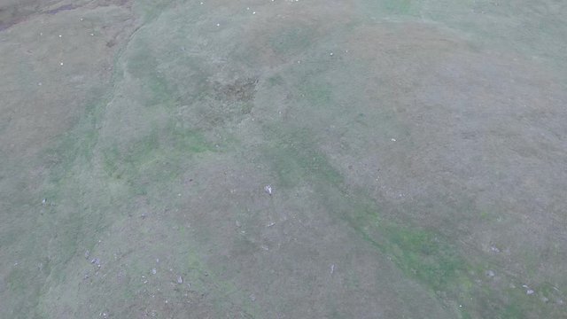 An aerial backward reveal footage of a grassy mountain rocky summit with small pond and mountain range in the background under a cloudy sky