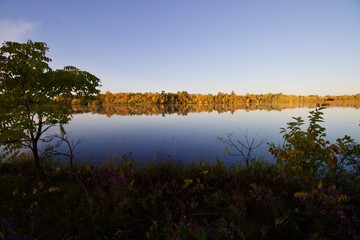 Fototapeta na wymiar Stunning fall foliage with reflection along a river bank lakeside at sunrise