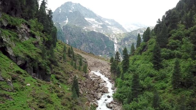 Wide angle aerial shot to a scenic valley with a huge waterfall in the background which is surrounded by mountains.