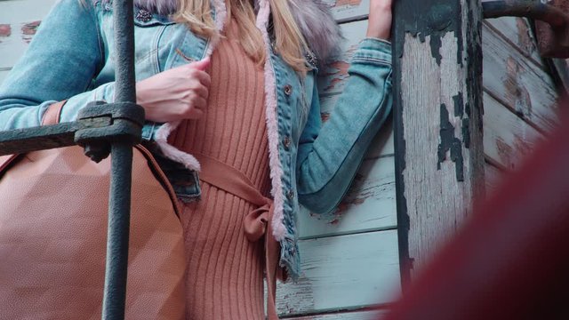 Headless female person with handbag posing in a jacket 4K. Long shot of person upper torso in focus holding a brown handbag.