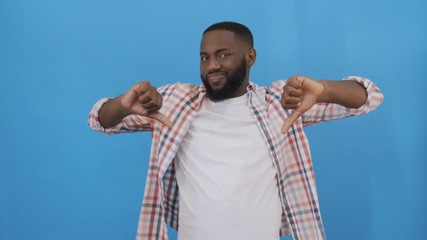 Close up emotional portrait of unhappy teen boy giving thumbs down hand gesture. Angry man looking with disapproval facial expression, isolated on blue background. Negative human face 4 k - Powered by Adobe
