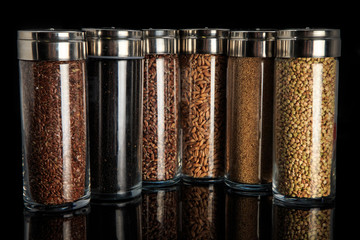 assorted organic groats in tall glass jars isolated on black
