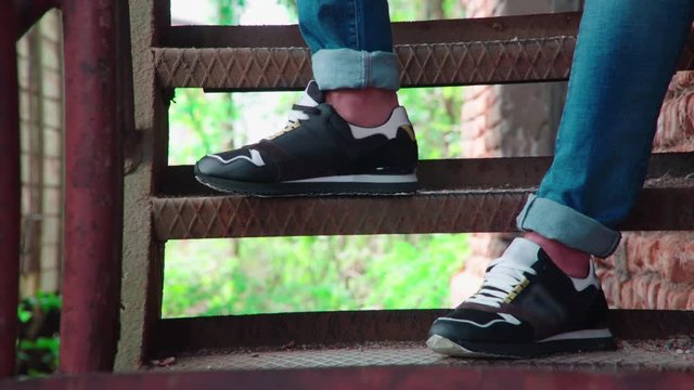 Long shot of person snickers on iron stairs 4K. Long shot dolly slide of casual snickers in focus with person stand on iron stairs.