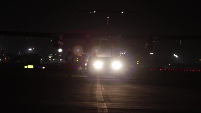 ATR propeller multi engine passenger aircraft towed at night by engineering crew airport lights in background