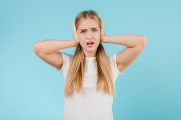 stressed young woman with headache covering ears isolated over blue