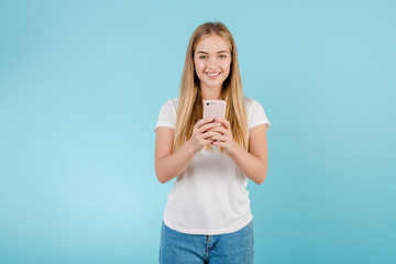 smiling young blonde woman looking at the phone isolated over blue