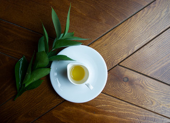 Spring honey with a white cup on a saucer with a green sprig on a wooden table.