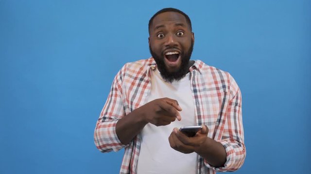 Surprised young man is holding phone and reading message pointing on it with finger 4K