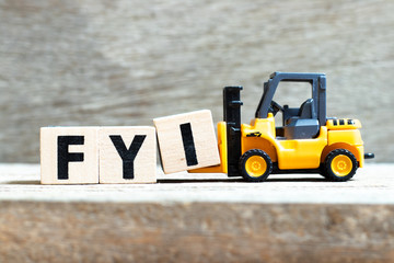 Toy forklift hold letter block I to complete word FYI (Abbreviation of For your information) on wood background