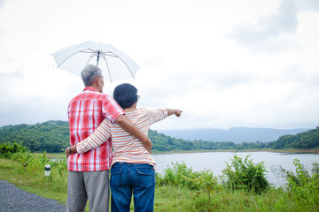 Elderly lovers standing together, husbands holding umbrellas for the wife is a lovely couple Stand to see the mountain view during the rainy season of the country. Elder community concept