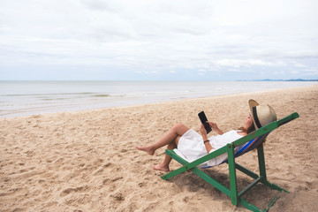 A woman holding and using tablet pc while laying down on a beach chair