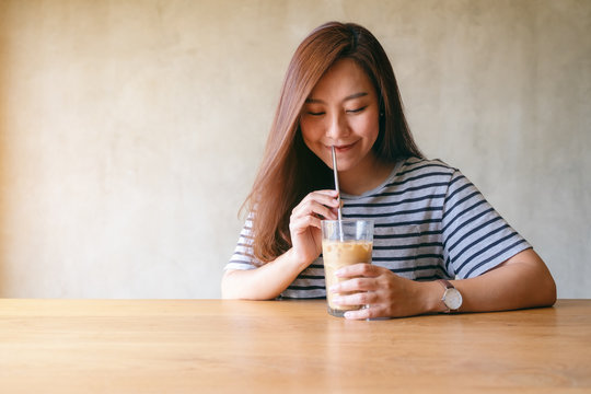 Closeup image of a beautiful asian woman drinking iced coffee with stainless steel straw
