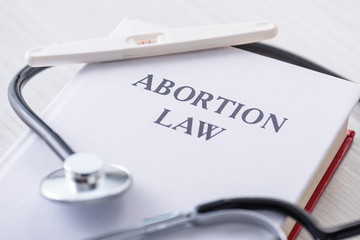 selective focus of pregnancy test on book with abortion law lettering near stethoscope