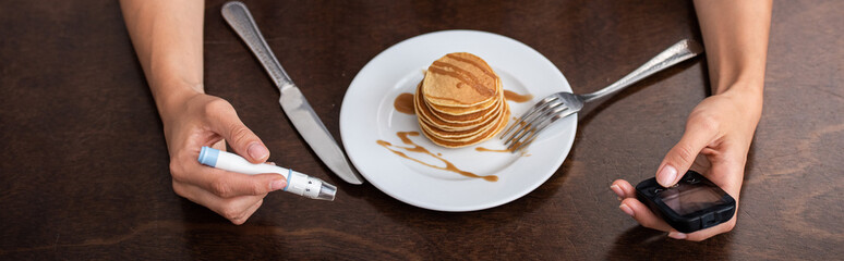 panoramic shot of woman holding blood lancet and glucose monitor near plate with tasty pancakes