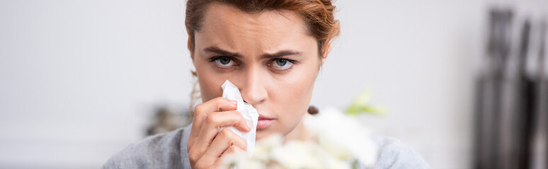 panoramic shot of sick woman with pollen allergy holding tissue near flowers