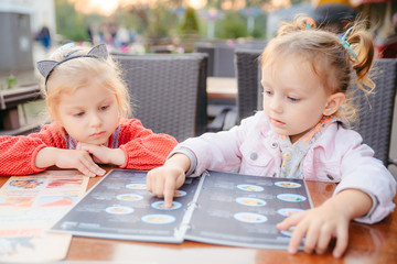 little girl sitting in cafe choosing food from menu