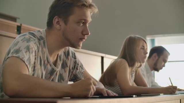 The camera moves through the class between the rows. University production a large audience, students write in the lecture notebooks and laptops