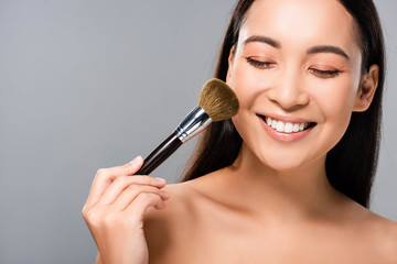 happy naked asian woman with cosmetic brush isolated on grey