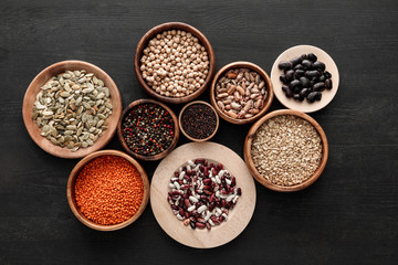 top view of various wooden plates and bowls with beans, cereals, spice and pumpkin seeds on dark wooden table