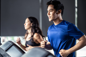 Young fit handsome Asian man and beautiful Asian woman running on treadmill or running machine in...