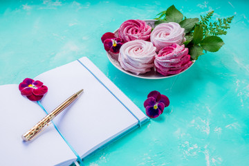 Flat lay with open book with empty pages,and pink meringues on concrete background. Overhead view, copy space. Blogger workplace.Sweet memories.Planning for future. Important thoughts.