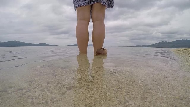A 60 fps video of a coconut drifting slowly next to a girl standing on the waters edge