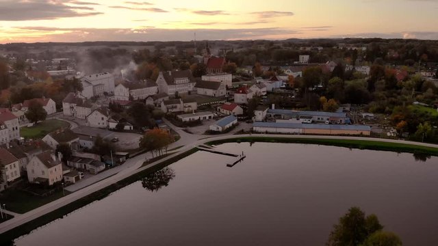 Aerial footage on the pond in the middle of the city, historic town in Poland, recreational path around the lake in the city, ancient buildings of the city, beautiful sunset in Warmia and Mazury
