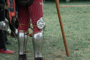 Knight stands on the grass, legs of a knight in armor close up,