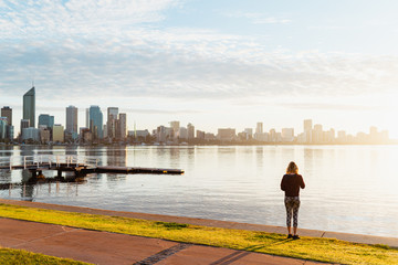 Fototapeta na wymiar Girl walking along the South Perth foreshore at sunrise, taking in the views of the city as the sun rises over the Swan river. 