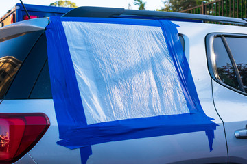 Close up. Broken and damaged car window temporarily covered with blue tape and plastic bag to...