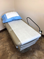 Medical Examination Table with disposable paper sheet and blue pillow cover in a doctor's office or clinic. Vertical image. - obrazy, fototapety, plakaty