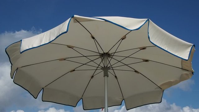 white beach umbrella viewed from above sways moved by the sea breeze . Blue sky with  white clouds background