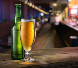Glass of light beer and green beer bottle on the bar counter.
