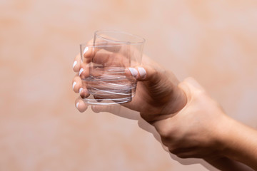 Closeup view on the shaking hand of a person holding drinking glass suffering from Parkinson's...