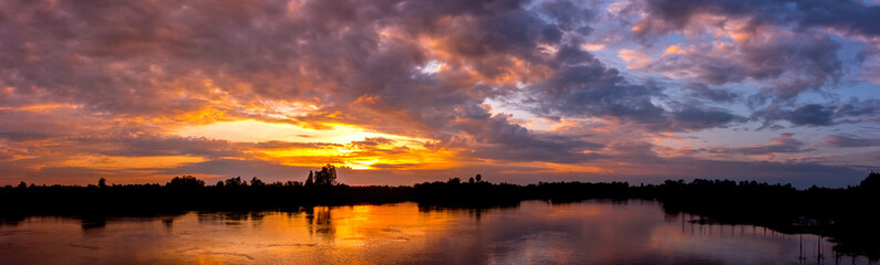 Obraz premium Panorama Reflection of vivid sunset sky reflection in water.Colorful sunrise with Clouds over Lake at Koh Klang nam , Sisaket province,Thailand,ASIA.