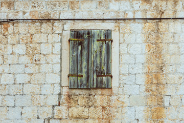 Fototapeta na wymiar Front view of an old mediterranean stone house with old dilapidated green wooden closed shutters, vintage toned
