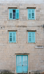 Street and front view of an old mediterranean stone house with turquoise doors and window shutters, typical mediterranean architecture, Vis island, Croatia, Europe. Summer travel concept.